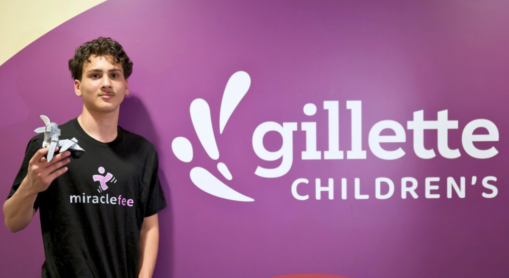 A teenage boy who was born with clubfoot poses by the hospital logo.